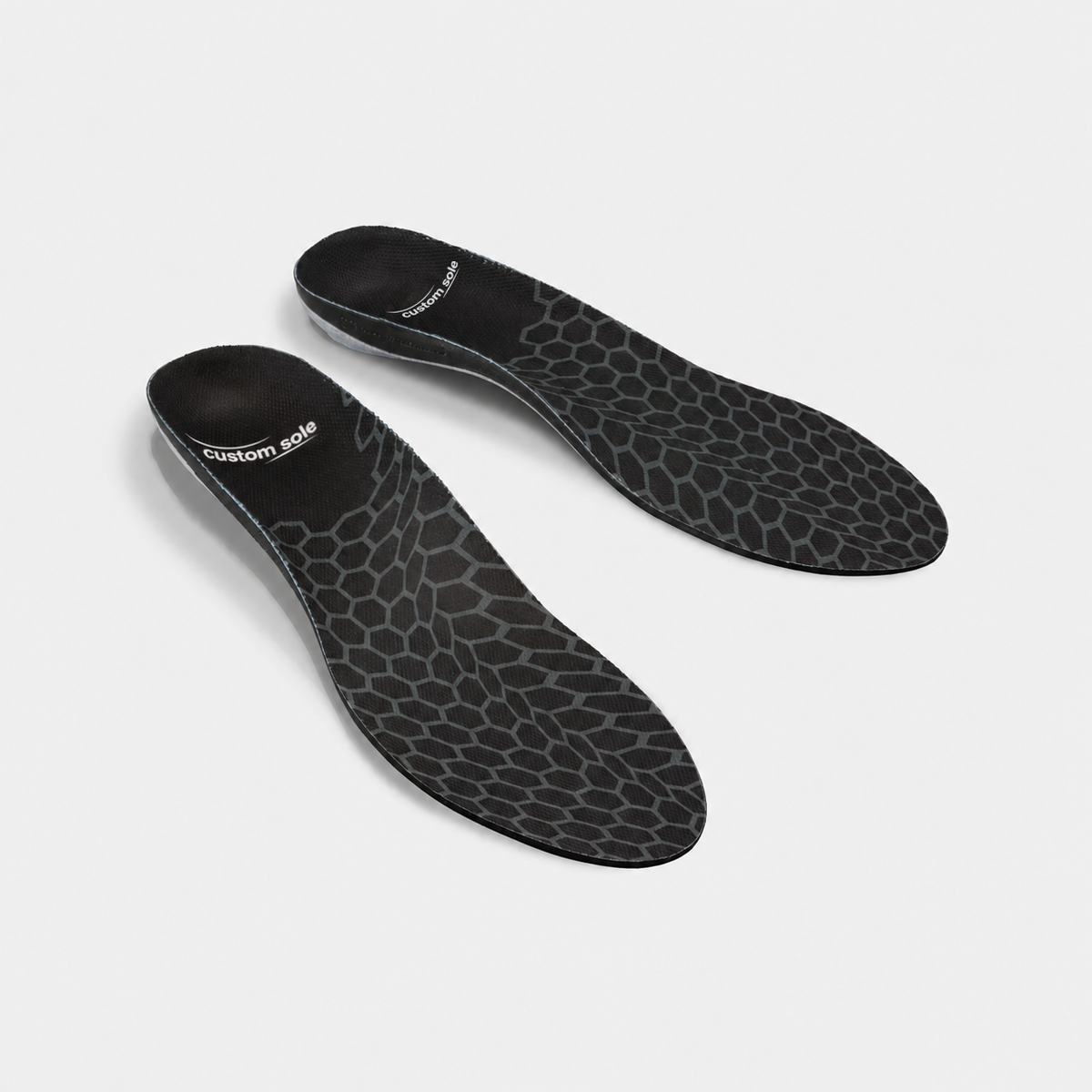 Carbon Cell custom insoles shown at an angle to reveal the contoured arch and deep heel cup: black knit cover with a grey hexagonal cell pattern and CustomSole logo at the heel